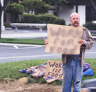 man standing by side of road with cardboard sign that says “Work for food”